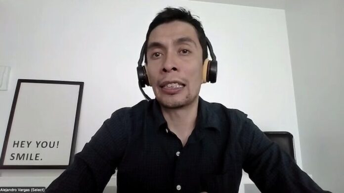 Primer plano del analista Alejandro Vargas, de la firma Select, hablando durante una videoconferencia en vivo. Viste una camisa oscura, lleva puestos unos auriculares de diadema negros y, al fondo a la izquierda, sobre la pared blanca, se observa un cuadro decorativo con la frase en inglés 