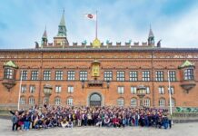 Convención CT 2026 navegará por Europa para fortalecer negocios y alianzas del canal TI Una gran fotografía grupal que reúne a decenas de distribuidores, fabricantes y directivos de CT Internacional posando sonrientes y saludando frente a la imponente fachada histórica de ladrillo rojo del Ayuntamiento de Copenhague. En la parte superior del edificio, ondea una bandera blanca con el logotipo de la empresa organizadora bajo un cielo parcialmente nublado.