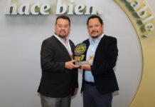 CT Internacional reafirma su compromiso social con 14 años consecutivos de reconocimiento Fotografía en plano medio de dos ejecutivos de pie, sosteniendo juntos una estatuilla con las siglas "ESR". El directivo de la izquierda viste un saco formal oscuro y pantalón gris, mientras que el de la derecha, Carlos Bautista, porta una camisa azul claro y saco negro. Al fondo se distingue una estructura circular beige con letras blancas en relieve donde se lee de forma parcial la frase "hace bien. ...sable".