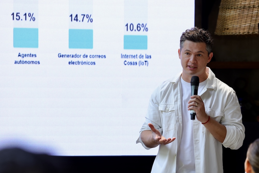 David Ortiz, CEO para Siigo Aspel Latam, explicando con micrófono en mano frente a una pantalla que proyecta una gráfica de barras con los porcentajes de adopción de agentes autónomos (15.1%), generadores de correos (14.7%) e Internet de las Cosas (10.6%).