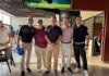 CVA acelera proyectos tecnológicos con una nueva estrategia de canales Cinco directivos y ejecutivos de Grupo CVA posan de pie, sonrientes y alineados en un área techada junto a un campo de golf durante un evento deportivo institucional. Visten ropa deportiva de golf con playeras tipo polo en tonos negro, guinda, azul marino y lila, pantalones claros y oscuros, gorras y tenis, situados al lado de un banner publicitario del torneo.