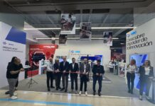 Centro de experiencia HP abre una nueva etapa para la experiencia tecnológica en retail Perspectiva general desde el pasillo comercial hacia la ceremonia de inauguración del Centro de Experiencia. En el centro, una fila de seis directivos de HP e Intel cortan de forma sincronizada una cinta roja delgada con tijeras plateadas, acompañados a la izquierda por dos fotógrafos que registran el evento y a la derecha por dos ejecutivas de relaciones públicas, una de ellas hablando por un micrófono. El stand blanco del fondo exhibe letreros con los títulos "Descubre el poder de la innovación" y "Centro de Experiencias" bajo los logotipos de ambas firmas.