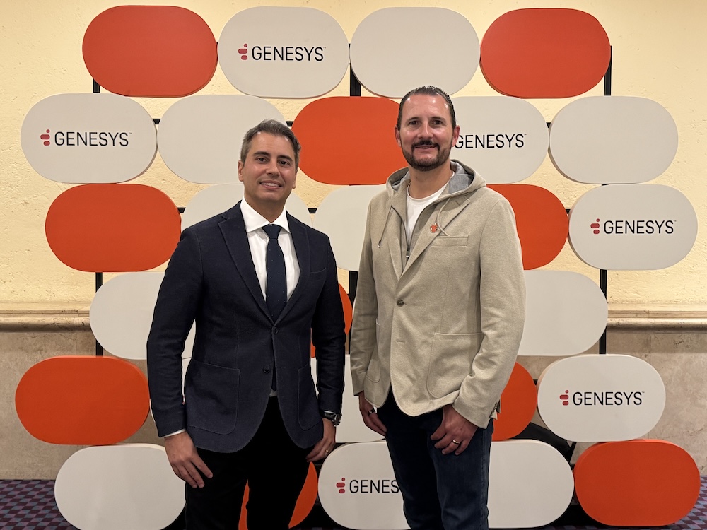 Rander Souza y Mauricio García, directivos de Genesys, posando juntos sonrientes frente a un mural decorativo con el logotipo de la compañía.
