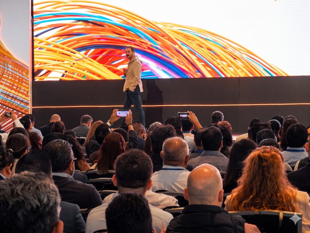 Ponente en el escenario principal del Xperience 2026 exponiendo ante un auditorio lleno, respaldado por una gran pantalla con gráficos de líneas de colores.