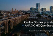 Carlos Gómez asume ANADIC MX Querétaro con una apuesta por fortalecer el ecosistema tecnológico regional Fotografía de paisaje urbano en perspectiva aérea nocturna de la ciudad de Santiago de Querétaro. A la izquierda se extiende el monumental Acueducto de Querétaro iluminado con luces cálidas, conectando con la arquitectura colonial de la zona histórica. A la derecha, se erigen rascacielos y edificios modernos con oficinas corporativas, entrelazados por un diseño gráfico digital de líneas cinéticas celestes que simulan una red de datos e infraestructura digital conectada. En el cuadrante inferior derecho, se superpone el texto en letras blancas: "Carlos Gómez preside ANADIC MX Querétaro - Liderando el canal tecnológico regional", acompañado del imagotipo azul de la asociación en el extremo inferior izquierdo de la frase.