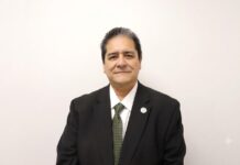 Grupo CVA fortalece servicios tecnológicos con alianza entre FMM y Masterchannel para proyectos TIC Fotografía de estudio en plano medio que muestra a Alberto Escamilla, Director General de Fulfillment Management México (FMM), posando de frente sobre un fondo completamente blanco. El directivo tiene tez clara y cabello corto oscuro con sutiles canas en las sienes, y viste un saco formal negro entallado sobre una camisa de vestir blanca y una corbata verde oliva con patrones geométricos sutiles. En la solapa izquierda de su saco resalta un pequeño pin metálico con el logotipo circular de la empresa, manteniendo los brazos sueltos a los costados y una mirada sutil frente a la cámara.