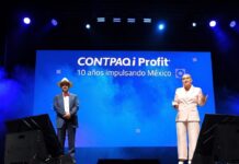 Profit 2026: CONTPAQi y Banorte aceleran digitalización financiera para PyMEs Fotografía completa tomada desde la base del escenario principal del auditorio, el cual se encuentra iluminado por reflectores superiores en tonos azules y blancos. En la tarima, René Torres posa a la izquierda con un traje azul marino, pajarita roja y sombrero de paja claro, mientras que Marlene García se ubica a la derecha exponiendo en un traje sastre formal de color rosa pálido con un apuntador digital en la mano. A sus espaldas, una pantalla gigante de color azul brillante proyecta en letras blancas el logotipo "CONTPAQi Profit® AÑOS IMPULSANDO MÉXICO" envuelto en efectos visuales de humo.