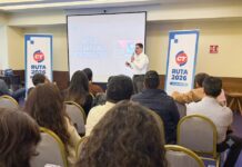 CT Internacional impulsa al canal TI con la Ruta CT Business & Training 2026 en el Bajío Fotografía que muestra una sala de conferencias con un conferencista de pie hablando frente a una audiencia sentada de espaldas. El ponente, un hombre de camisa blanca y pantalón oscuro, sostiene un micrófono inalámbrico. A los lados de la pantalla de proyección se ubican dos tótems publicitarios azules con el logotipo de CT Internacional y la leyenda "RUTA 2026". En la pantalla se proyecta una presentación con el título "MITO 2: LOS ANTIVIRUS SON OBSOLETOS" al lado del imagotipo de la marca ESET.