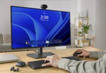 Dell lanza webcams con IA y reconocimiento facial 4K y 2K para trabajo híbrido Fotografía de estudio con fondo blanco que muestra la cámara web Dell Pro 5 Webcam 2K (WB526) vista de frente y montada sobre un soporte de clip negro. El dispositivo tiene un diseño cilíndrico compacto de color negro mate con un lente central circular de vidrio texturizado y un pequeño indicador LED a la izquierda. El soporte inferior articulado permite fijar la cámara de manera segura sobre el borde superior de un monitor de computadora o pantalla de portátil.