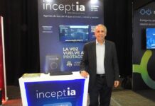 IA conversacional: Inceptia apuesta por los canales para acelerar la automatización empresarial Fotografía en plano general medio de Gustavo Capart, CEO de Inceptia, posando de frente y sonriente junto al stand corporativo de su empresa durante el evento América Digital MX 2026. El directivo tiene cabello corto canoso, tez clara y viste un traje formal con saco gris oscuro sobre una camisa de vestir azul claro de cuello abierto, sin corbata, y pantalón oscuro. Apoya su mano derecha sobre un mostrador blanco retroiluminado con luces LED de color azul brillante que muestra el logotipo de "Inceptia INTELIGENCIA ARTIFICIAL" y el enlace web de su plataforma. Al fondo, la mampara publicitaria exhibe gráficos digitales de asistentes virtuales bajo el lema "Agentes de voz con IA que atienden, cobran y venden".