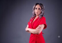 CANACINTRA impulsa transformación digital empresarial en 2026 Retrato corporativo de estudio en plano medio de tres cuartos hacia la izquierda de Haydée Arámbula, Presidenta del Sector Tecnologías para la Información y Economía del Conocimiento (TIEC) en CANACINTRA. Posa con los brazos cruzados, vistiendo un vestido formal texturizado de color rojo intenso con cuello tipo sastre. Tiene el cabello ondulado de largo medio en tonos castaños y grises, y se encuentra de pie frente a un fondo de estudio gris liso y neutro.