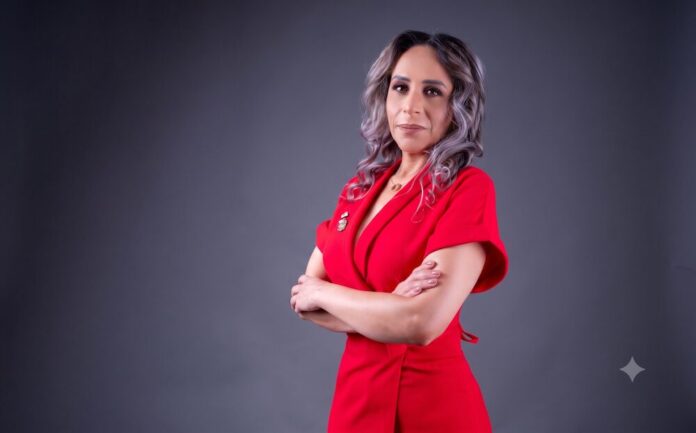 Haydée Arámbula delinea las estrategias transversales para democratizar la digitalización en las PyMEs Retrato corporativo de estudio en plano medio de tres cuartos hacia la izquierda de Haydée Arámbula, Presidenta del Sector Tecnologías para la Información y Economía del Conocimiento (TIEC) en CANACINTRA. Posa con los brazos cruzados, vistiendo un vestido formal texturizado de color rojo intenso con cuello tipo sastre. Tiene el cabello ondulado de largo medio en tonos castaños y grises, y se encuentra de pie frente a un fondo de estudio gris liso y neutro.