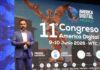 Transformación digital e inteligencia artificial redefinen los negocios en América Digital 2026 Fotografía en plano medio largo que muestra a Lesley Robles, director de América Digital, de pie pronunciando una conferencia magistral sobre un escenario. Viste un traje formal azul de cuadros discretos, camisa blanca de cuello abierto y sostiene un apuntador digital en su mano. Detrás de él, la enorme pantalla de proyección exhibe un fondo con la silueta dorada del Ángel de la Independencia, el título "11° Congreso América Digital - 9-10 Junio 2026 • WTC" y métricas que detallan "+5000 asistentes", "+200 expositores" y "+22 países", acompañadas por íconos de verticales tecnológicas en la base.