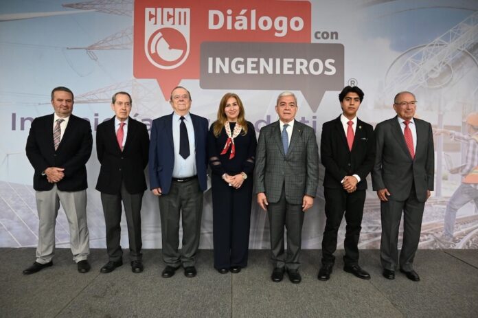 Fotografía en plano general que muestra a siete profesionales en fila posando de pie en un presídium frente a un gran panel publicitario. En el muro de fondo resalta un gráfico rojo en forma de bocadillo de diálogo con las siglas 