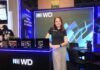 Western Digital: almacenamiento empresarial interno seguro y escalable Fotografía de tres cuartos de Sandra Mendoza, gerente de Mercadotecnia para Latinoamérica en Western Digital, posando de pie con una sonrisa frente a un stand corporativo. Viste una playera polo negra con el logotipo de WD y pantalones de vestir color gris claro. A su izquierda, sobre un mostrador negro con luz LED azul perimetral, se encuentran en exhibición tres discos duros Ultrastar. A su espalda, un gran panel vertical muestra el mensaje "ALMACENAMIENTO PARA ADAPTARSE AL MAÑANA", acompañado de una mesa redonda negra con sillas de terciopelo en el lado derecho del encuadre.