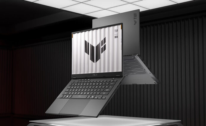 Imagen renderizada que muestra dos laptops ASUS TUF Gaming A14 en color gris oscuro flotando sobre un panel iluminado dentro de un entorno oscuro con paredes metálicas. La computadora principal aparece abierta en primer plano, mostrando el teclado, el touchpad y la pantalla con el logotipo de TUF sobre un fondo blanco estriado. La segunda computadora flota detrás, mostrando la tapa exterior con el emblema de la marca y el diseño de la rejilla de ventilación en la base.