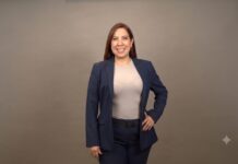 HiRef apuesta por la IA para reducir la huella ambiental de los Centros de Datos Fotografía de medio cuerpo de una mujer sonriente de cabello castaño rojizo, vistiendo un traje sastre azul marino y blusa color arena, posando con la mano izquierda en la cadera frente a un fondo gris neutro.
