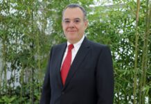Sandisk explica por qué el almacenamiento flash será la base de la era de la IA física Retrato corporativo de plano medio de Eduardo Alexandri, director general de SanDisk para América Latina. El directivo, de tez clara y con anteojos, viste un traje formal oscuro, camisa blanca y corbata roja texturizada. Posa de frente con una ligera sonrisa ante un fondo natural compuesto por tallos y hojas de bambú verde brillante.