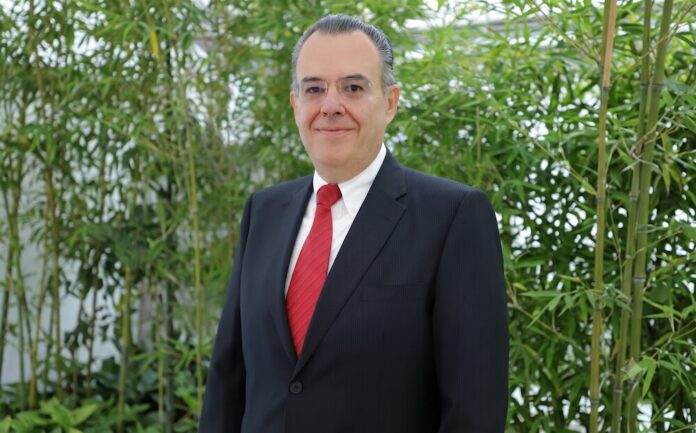 Retrato corporativo de plano medio de Eduardo Alexandri, director general de SanDisk para América Latina. El directivo, de tez clara y con anteojos, viste un traje formal oscuro, camisa blanca y corbata roja texturizada. Posa de frente con una ligera sonrisa ante un fondo natural compuesto por tallos y hojas de bambú verde brillante.