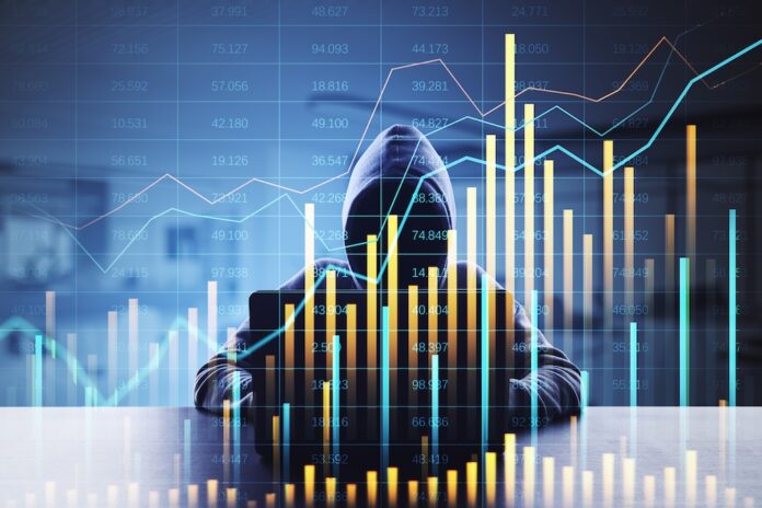 El cibercrimen como servicio. La tercera economía mundial y su impacto en Latinoamérica Silueta de una persona encapuchada trabajando frente a una computadora portátil en un ambiente con poca iluminación. Sobre la figura y el fondo se superponen múltiples gráficos bursátiles luminosos, líneas de tendencia fluctuantes y diagramas de barras con cifras numéricas, lo que ilustra visualmente el concepto de la rentabilidad financiera y el ecosistema económico de los ataques digitales.