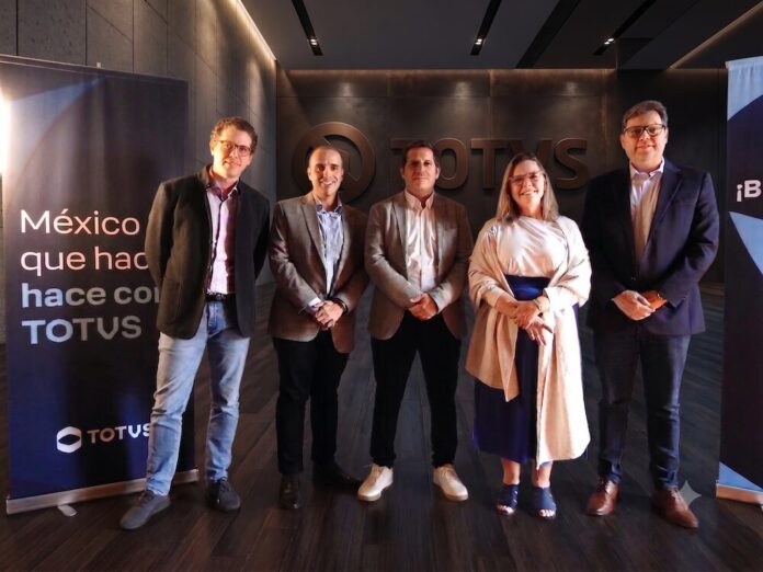 Fotografía grupal de los cinco ejecutivos de TOTVS parados de izquierda a derecha: Marcelo Cosentino, Elói Assis, Javier Marbec, Vivian Broge e Ivaldo Pereira. Todos lucen vestimenta ejecutiva y sonríen frente a un fondo corporativo iluminado con la frase 