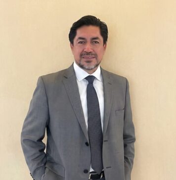 HD Latinoamérica impulsa oportunidades de negocio en ciberseguridad para el canal en Puebla Retrato de estudio en plano medio y de frente de Fausto Escobar, CEO de HD Latinoamérica, posando de pie con una sutil sonrisa y las manos en los bolsillos de su pantalón. El ejecutivo, de tez morena clara, cabello oscuro y barba corta de candado bien recortada, viste un saco de traje formal color gris, una camisa de vestir blanca de cuello rígido y una corbata de color gris oscuro texturizada, situado ante un muro liso de fondo beige claro.