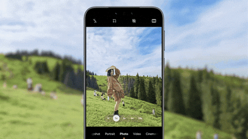 Animación de la pantalla de un teléfono móvil utilizando la interfaz de la cámara fotográfica. La lente enfoca a una mujer posando alegremente de perfil en medio de un campo verde y montañoso bajo un cielo azul.