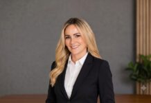 Laura Gómez impulsará una nueva etapa para el ecosistema de canales de HPE México Retrato corporativo de plano medio de Laura Gómez, quien posa sonriente mirando directamente a la cámara. La ejecutiva, de largo cabello rubio con ondas suaves, viste un saco negro formal sobre una camisa blanca de cuello. El fondo sutilmente desenfocado muestra un ambiente de oficina moderno con una pared gris texturizada, un panel arquitectónico de madera acanalada a la derecha y una pequeña planta verde decorativa sobre un escritorio de madera en primer plano.