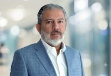 iTech apuntala la transformación empresarial con SAP para acelerar la innovación Fotografía de retrato de Manuel Bravo, director comercial de iTech. Es un hombre de mediana edad con cabello y barba entrecanos, que mira fijamente a la cámara con una expresión serena y profesional. Viste una camisa blanca desabotonada en el cuello y un saco de traje en tono azul claro con un sutil patrón de cuadros. El fondo se encuentra completamente desenfocado, mostrando luces y tonos claros que sugieren un entorno corporativo moderno.