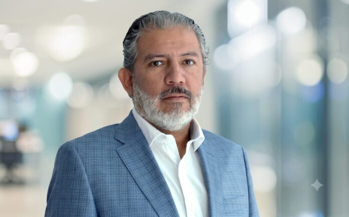 Manuel Bravo. Liderando la nueva era de la transformación empresarial con SAP Fotografía de retrato de Manuel Bravo, director comercial de iTech. Es un hombre de mediana edad con cabello y barba entrecanos, que mira fijamente a la cámara con una expresión serena y profesional. Viste una camisa blanca desabotonada en el cuello y un saco de traje en tono azul claro con un sutil patrón de cuadros. El fondo se encuentra completamente desenfocado, mostrando luces y tonos claros que sugieren un entorno corporativo moderno.