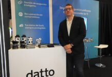 Kaseya impulsa una plataforma de ciberseguridad para empresas y fortalece la protección integral Retrato de Mateo Bolívar, gerente comercial de nuevos negocios para Latinoamérica en Kaseya, quien posa de frente con las manos entrelazadas a la altura de la cintura. El ejecutivo usa anteojos y viste un saco oscuro sobre una camisa clara y jeans. Se encuentra de pie junto a un mostrador blanco de la marca Datto, respaldado por un panel informativo azul que destaca beneficios como "Gestión de endpoints inteligente" y "Recuperación sin compromisos".