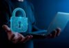 Nutanix fortalece la gobernanza de agentes de IA con mayor control de acceso y costos Ilustración conceptual de un especialista en tecnología sosteniendo una computadora portátil abierta con la mano derecha, mientras de su mano izquierda emerge un gran candado holográfico tridimensional de color azul brillante, estructurado con líneas de circuitos electrónicos y un resplandor luminoso en el centro.