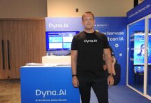 Dyna.Ai revoluciona la IA para contact center con agentes de voz inteligentes Fotografía en plano medio que muestra a Peter Dallen, presidente para América Latina de Dyna.Ai, posando de frente con una postura firme y formal en el espacio de exhibición de su compañía. El directivo, de tez clara y complexión robusta, viste una playera negra lisa con el logotipo blanco de "Dyna.Ai" al centro del pecho y un pantalón de vestir oscuro, complementado con un reloj y una pulsera negra en sus muñecas. Detrás de él resalta un mostrador azul con folletos corporativos y una pantalla digital que despliega la ponencia "Las plataformas basadas en flujos de trabajo ya no pueden seguir el ritmo".