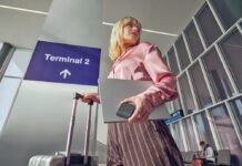 Logitech Mobi Fold lleva la productividad a cualquier lugar con un innovador mouse plegable Fotografía en contrapicado de una mujer rubia en un aeropuerto frente a un letrero que dice "Terminal 2". La mujer sostiene una laptop plateada cerrada junto con un dispositivo cuadrado y compacto de color oscuro en una mano, mientras con la otra sujeta el asa de una maleta de viaje plateada.