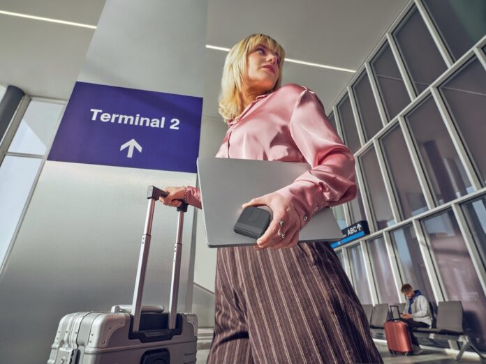 Fotografía en contrapicado de una mujer rubia en un aeropuerto frente a un letrero que dice 