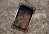 ML Rugged presenta la familia Jaeger con tablets industriales IP68 para operaciones en campo Fotografía de producto en condiciones reales de uso que muestra la pantalla frontal de la tableta Jaeger 8A de ML Rugged recostada de forma diagonal sobre un terreno lodoso, húmedo y con piedras sueltas. La superficie de la pantalla de cristal templado y los bordes con detalles naranjas y blancos del chasis reforzado se encuentran severamente cubiertos por salpicaduras densas de lodo marrón oscuro, mientras que a la derecha, en la tierra mojada, se distingue la huella de una bota de trabajo industrial.