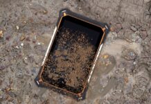 ML Rugged presenta la familia Jaeger con tablets industriales IP68 para operaciones en campo Fotografía de producto en condiciones reales de uso que muestra la pantalla frontal de la tableta Jaeger 8A de ML Rugged recostada de forma diagonal sobre un terreno lodoso, húmedo y con piedras sueltas. La superficie de la pantalla de cristal templado y los bordes con detalles naranjas y blancos del chasis reforzado se encuentran severamente cubiertos por salpicaduras densas de lodo marrón oscuro, mientras que a la derecha, en la tierra mojada, se distingue la huella de una bota de trabajo industrial.
