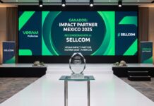 Sellcom obtiene el reconocimiento Impact Partner Mexico 2025 de Veeam Fotografía de un elegante escenario de premiación. En primer plano, un trofeo geométrico de cristal descansa sobre una mesa transparente. De fondo, una gran pantalla iluminada en tonos verdes y azules anuncia en letras blancas: "GANADOR: IMPACT PARTNER MEXICO 2025", "RECONOCIMIENTO A: SELLCOM" y "VEEAM IMPACT PARTNER AWARDS 2025 | AMERICAS". A los costados del escenario alfombrado se observan pendones corporativos con los logotipos de Veeam y Sellcom.