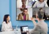 ViewSonic fortalece la ciberseguridad empresarial con su nueva serie CDEG3 de pantallas 4K Fotografía de dos profesionales en una sala de reuniones con paredes azules. Un hombre, visto de espaldas, gesticula con la mano derecha hacia una gran pantalla montada en la pared que muestra una videoconferencia con cuatro participantes. En la mesa blanca frente a él hay una computadora portátil conectada por cable, la cual muestra gráficos y datos en su pantalla. A su izquierda, una mujer con blusa blanca sonríe mientras presta atención a la reunión virtual.