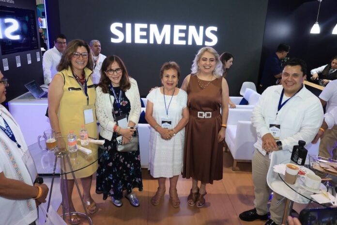 Fotografía grupal de cinco personas posando sonrientes frente a un gran letrero luminoso con la marca 