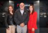 Kingston encuentra nuevas oportunidades para el canal ante los incrementos y desabasto del mercado Fotografía grupal de tres ejecutivos posando juntos en un entorno corporativo de exhibición tecnológica. De izquierda a derecha: Cristina Carbajal con chamarra negra, Oscar Martínez al centro con chamarra gris oscura, e Ivette Barragán vistiendo un traje rojo brillante, todos frente a vitrinas y pantallas de productos Kingston.