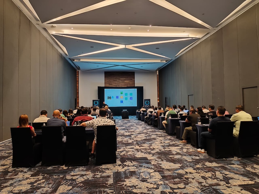 Fotografía de una sala de conferencias donde un grupo de asistentes sentados observa a un presentador que muestra un diagrama de flujo en una pantalla principal al fondo del salón.