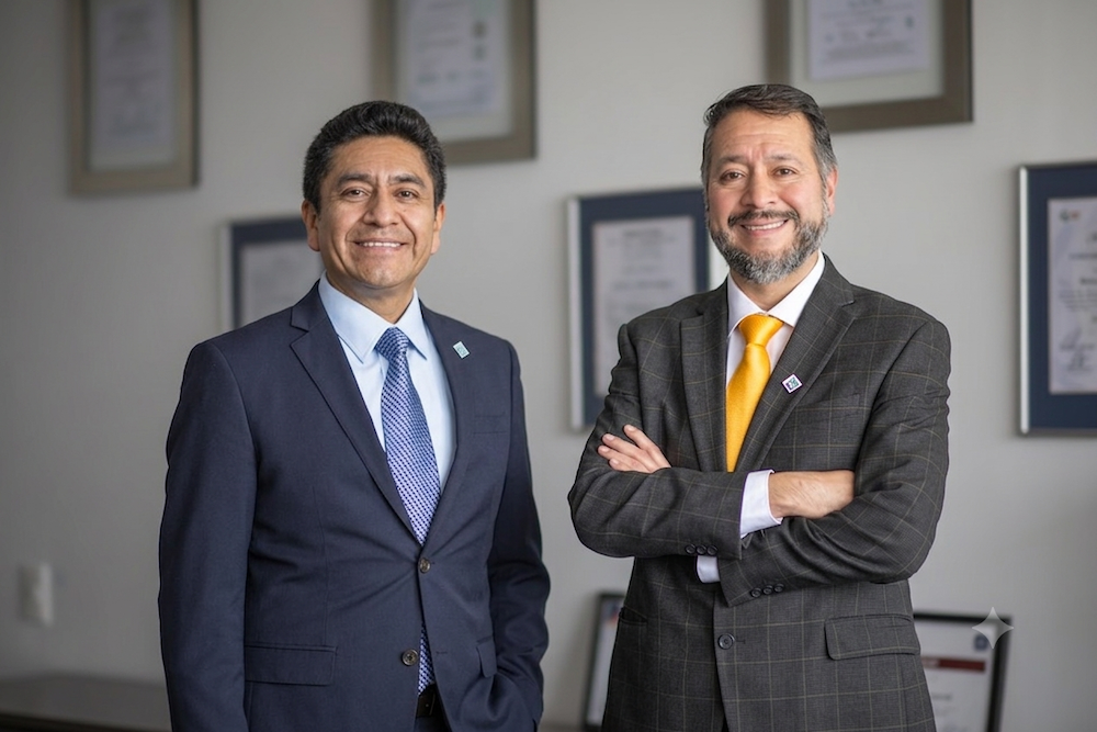 Cuatro décadas de experiencia impulsando la transformación digital Fotografía conjunta de Ángel Baños Carrillo y Julio Olmos posando uno al lado del otro. Ambos ejecutivos visten traje y corbata, y sonríen a la cámara de pie frente a una pared de tonos claros adornada con diplomas enmarcados.
