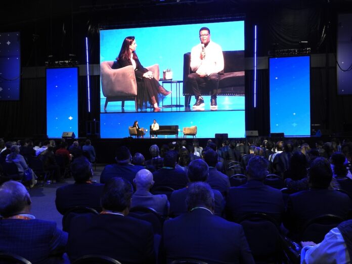 Vista desde la perspectiva del público hacia el escenario principal de SAP Now, donde se proyecta en pantallas gigantes la charla entre Adriana Aroulho y el CIO de Coca-Cola FEMSA, frente a una gran audiencia.