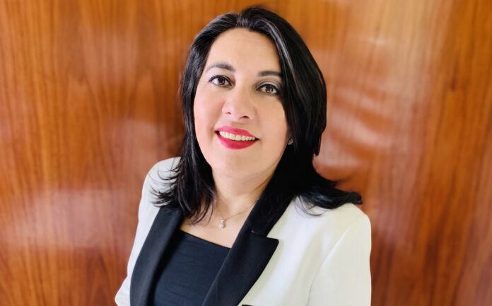 El nuevo rol estratégico de la regulación de energía en los negocios Fotografía de retrato de Gisela Rodríguez, directora general de Datashield. Ella aparece sonriendo a la cámara, con cabello oscuro hasta los hombros, vistiendo una blusa negra y un saco blanco con solapas negras, frente a un fondo de madera pulida.