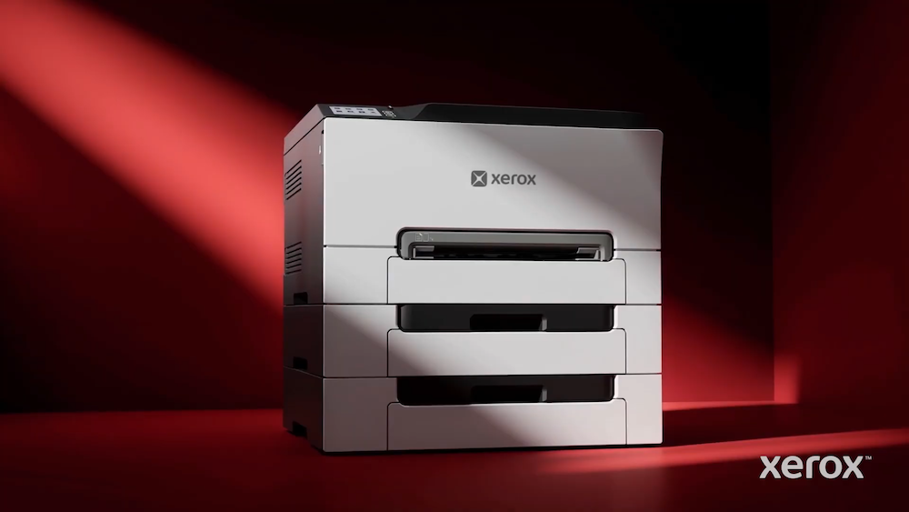 Fotografía de producto que muestra una impresora Xerox de alta capacidad con múltiples bandejas de papel apiladas. El equipo está iluminado por un haz de luz diagonal que resalta su diseño sobre un fondo de color rojo intenso y dramático.