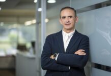 Hitachi Vantara fortalece al canal con soluciones de ciberresiliencia Fotografía de César Zurita, director comercial de Hitachi Vantara, posando en un entorno corporativo con los brazos cruzados. Viste un saco azul marino y camisa blanca sin corbata, apoyándose de forma relajada contra una pared de cristal en los pasillos de una oficina.