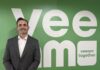 Veeam fortalece su estrategia en México con el nombramiento de Fernando Zambrana como Country Manager Fotografía de Fernando Zambrana sonriendo de frente a la cámara, vistiendo un saco gris texturizado y una camisa blanca sin corbata. Se encuentra de pie frente a un gran muro de color verde que muestra la palabra "Veeam" en letras blancas gigantes y el lema "veeam together".