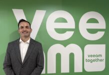 Veeam fortalece su estrategia en México con el nombramiento de Fernando Zambrana como Country Manager Fotografía de Fernando Zambrana sonriendo de frente a la cámara, vistiendo un saco gris texturizado y una camisa blanca sin corbata. Se encuentra de pie frente a un gran muro de color verde que muestra la palabra "Veeam" en letras blancas gigantes y el lema "veeam together".