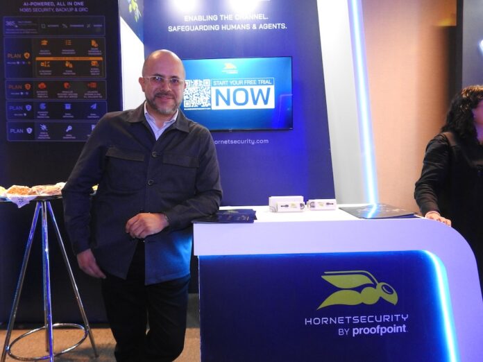 Fotografía de Alejandro Rodríguez, territory senior manager de Hornetsecurity, de pie frente a un stand de exhibición azul con el logotipo de Hornetsecurity by proofpoint.